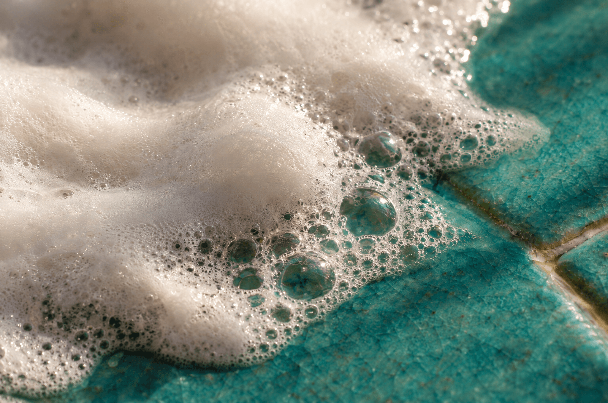 Soft white soap lather and small bubbles on a turquoise glazed tile.